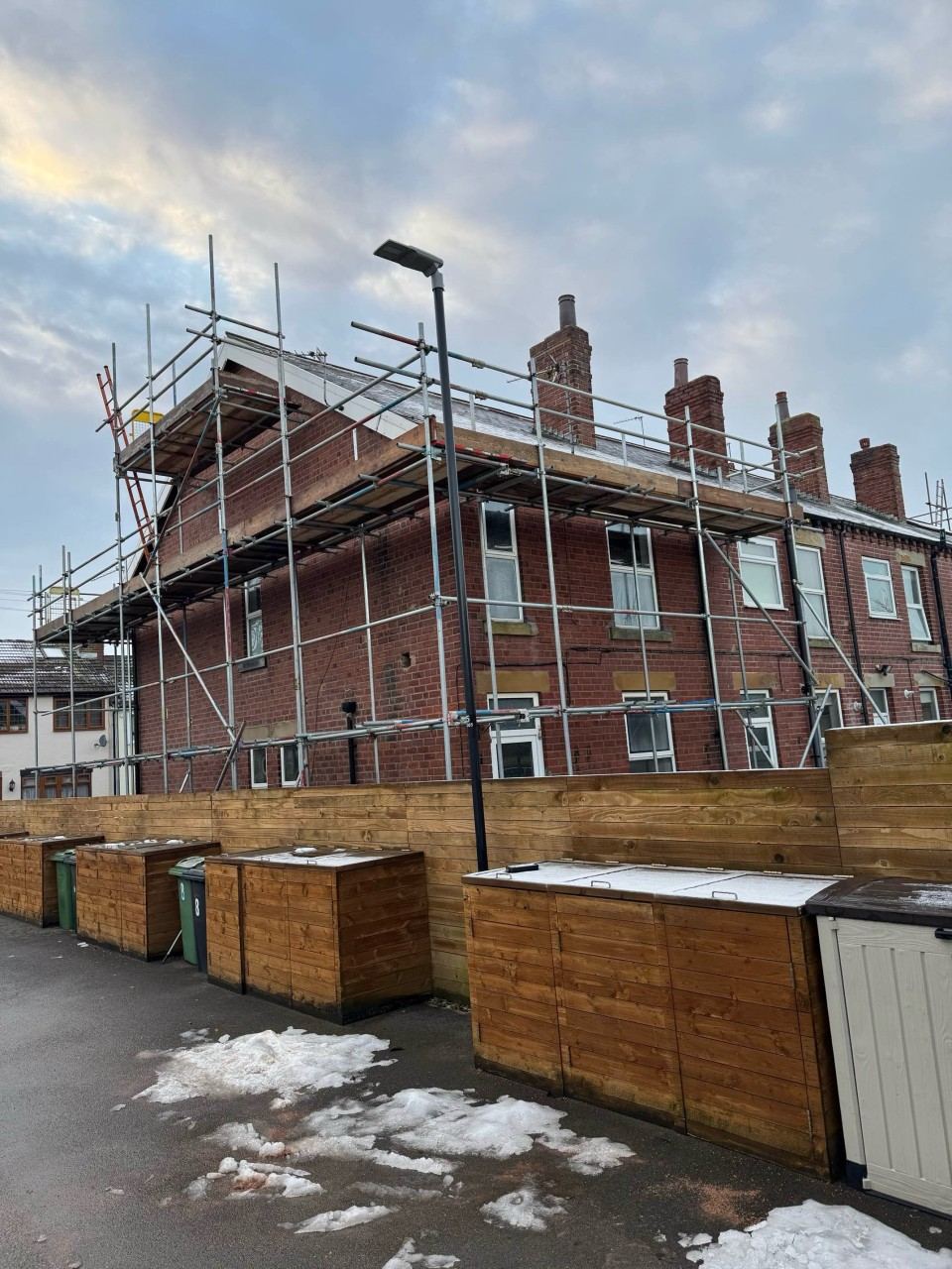 Scaffold around a red-brick end-terrace with hoarding at ground level