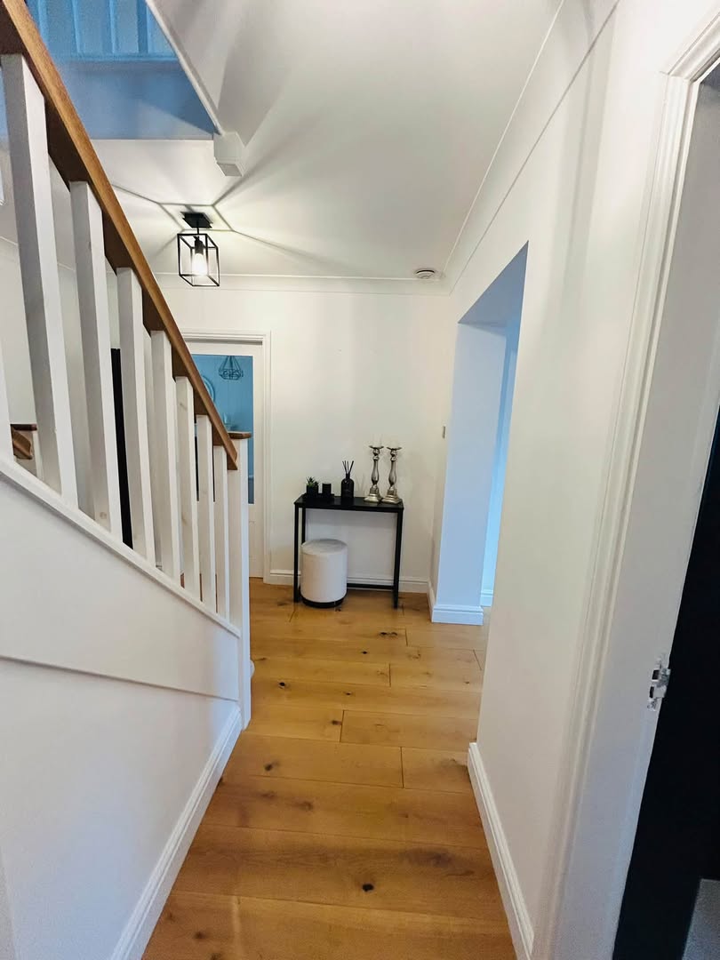 A bright hallway with a white painted staircase, white walls and a warm oak floor.