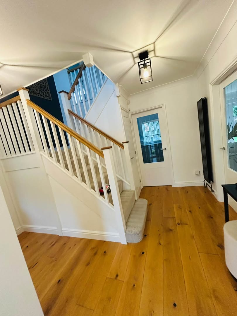 A staircase and hallway with white painted spindles and woodwork against a dark painted feature wall, warm oak floor.