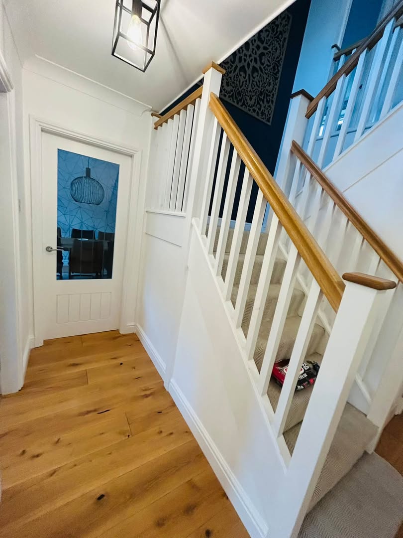 A painted staircase with white spindles and an oak handrail, beside a glazed front door.