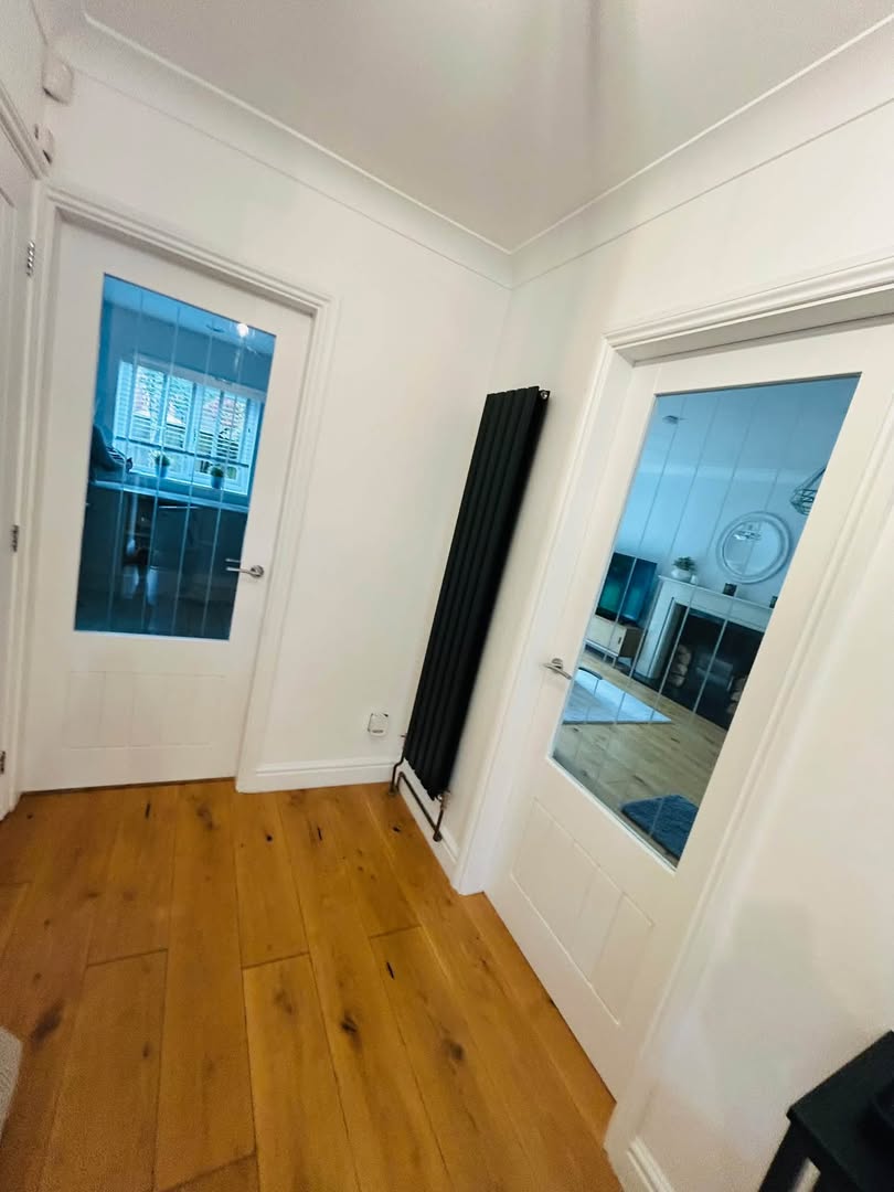 A white hallway with glazed internal doors, a dark radiator and an oak floor.