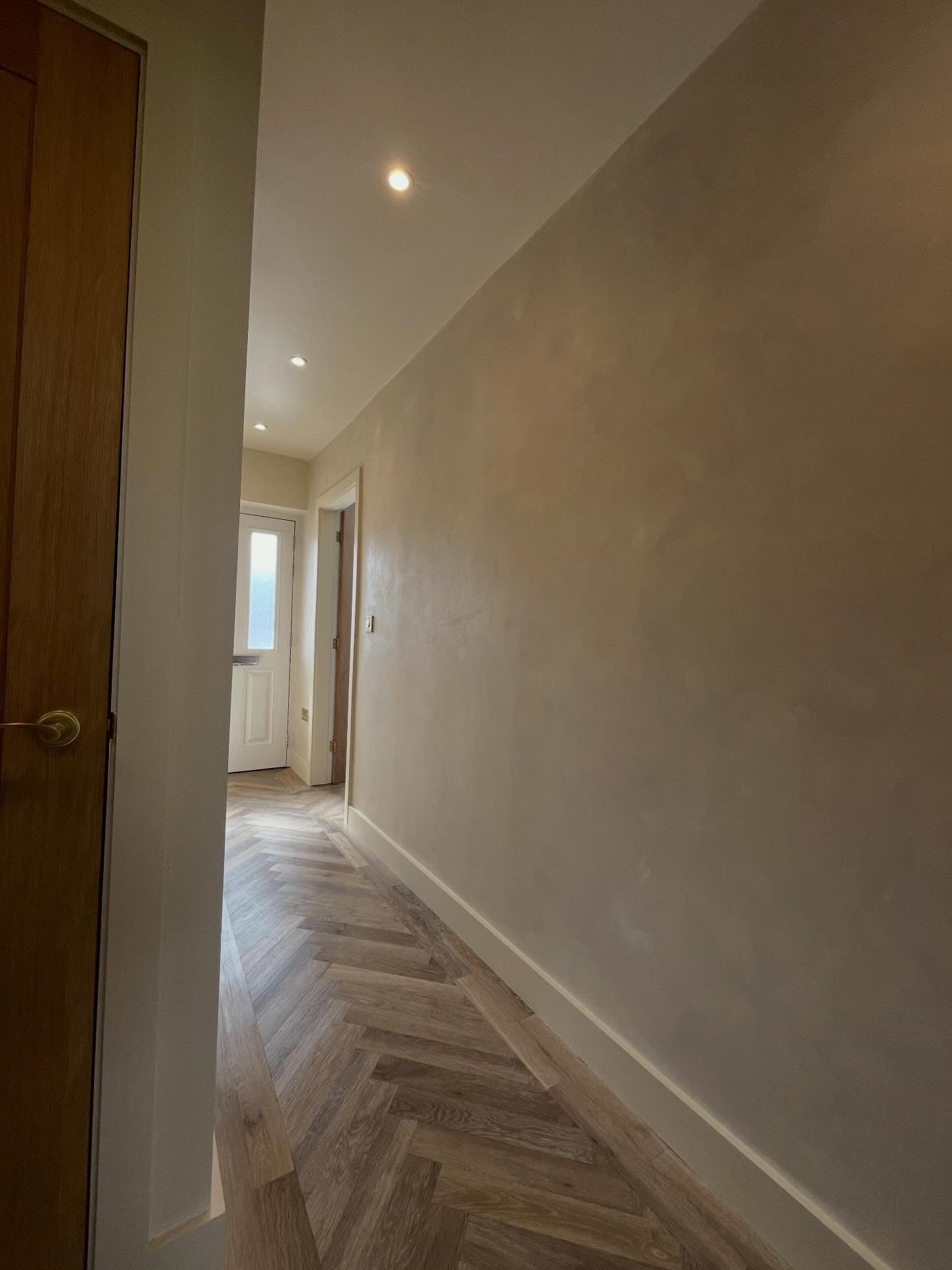 Lime wash effect feature wall in a hallway with herringbone floor